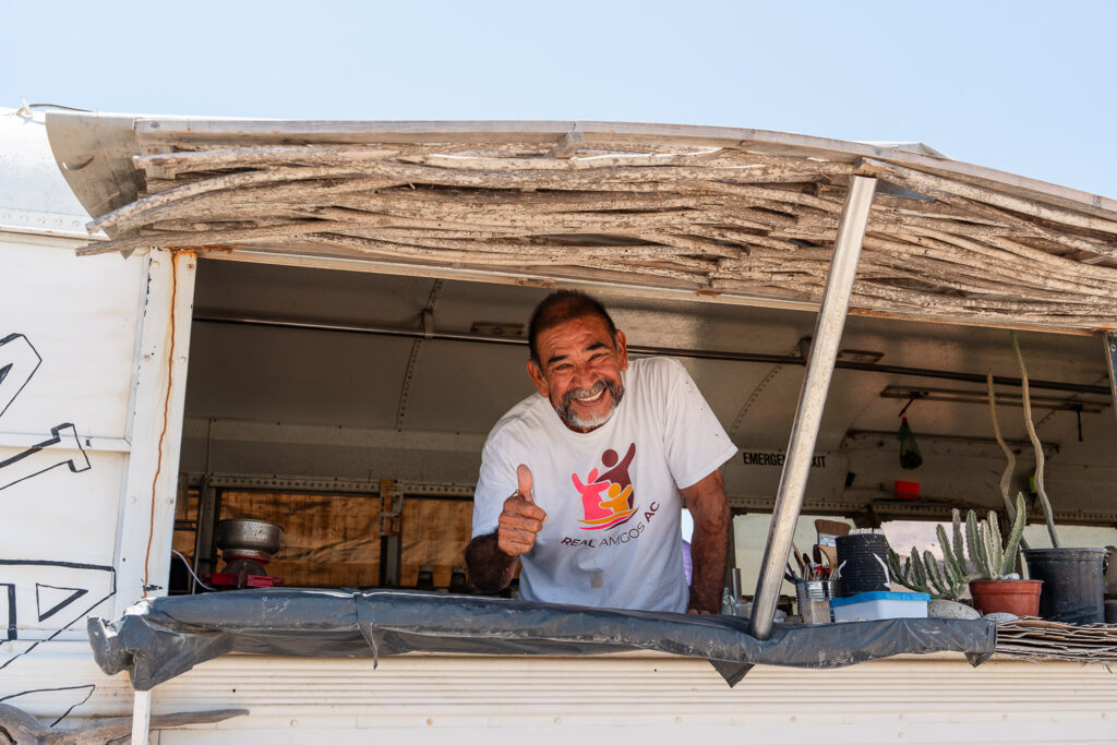 Owner and chef, Victor smiling from his taco stand inside a white bus called Restaurante La Fortuna.